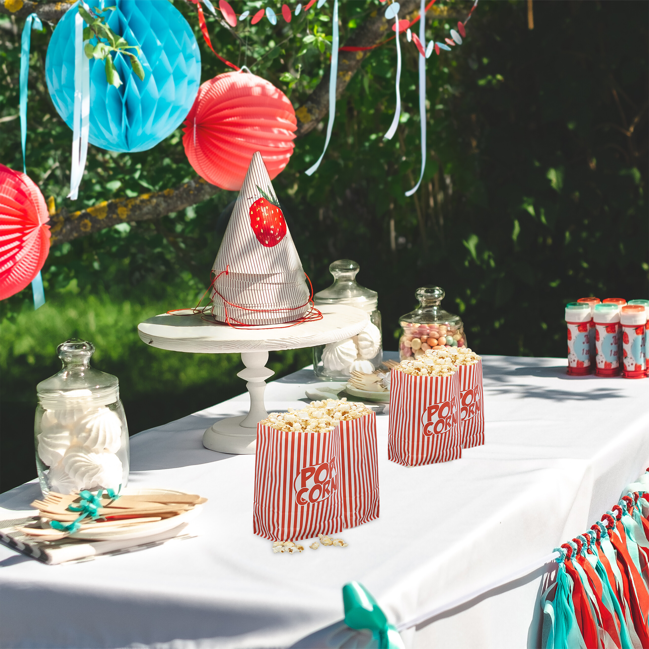 Ein Outdoor-Geburtstagstisch mit Popcorn, Süßigkeiten und bunten Dekorationen im Garten.