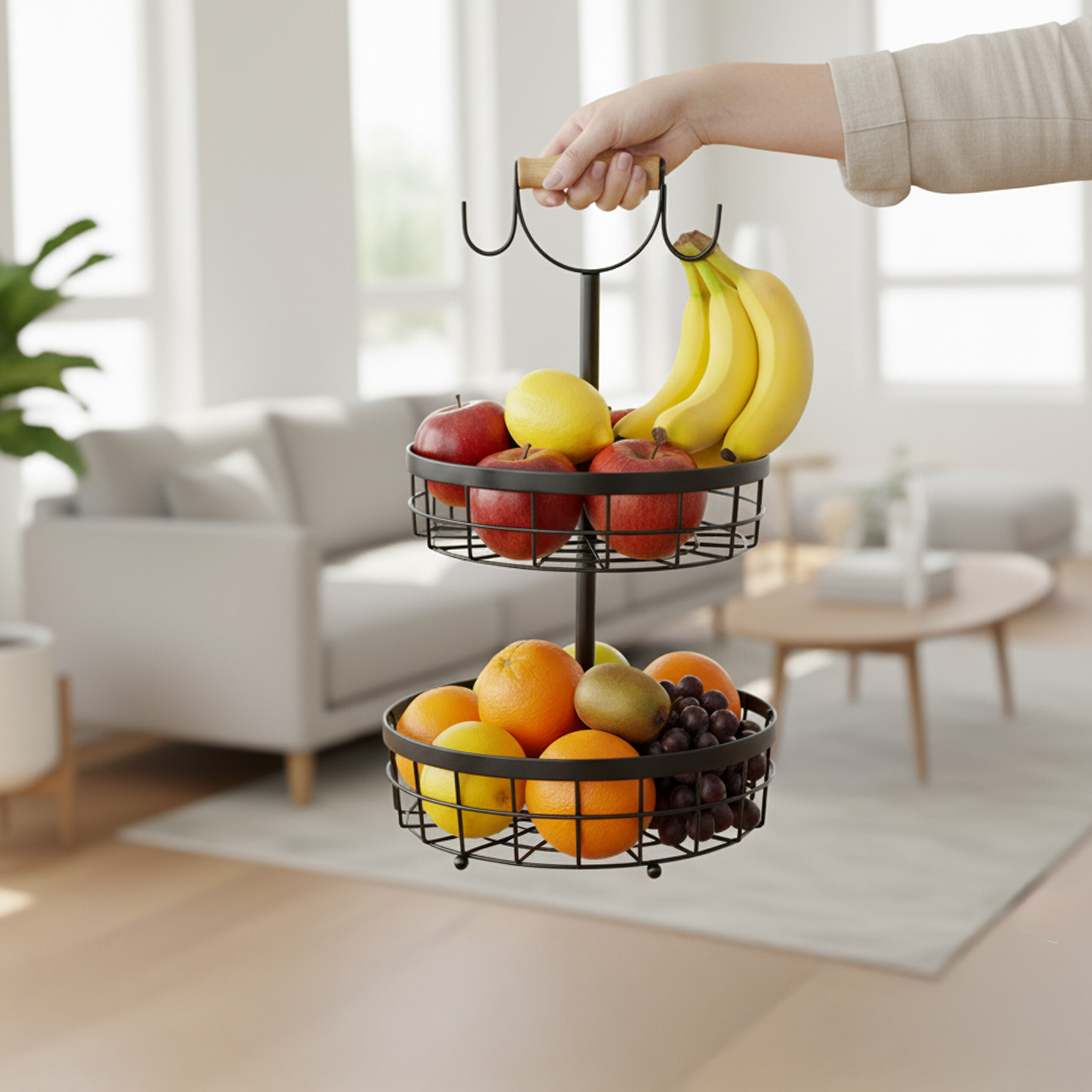 Eine Person hält einen zweistöckigen schwarzen Obstkorb mit Äpfeln, Bananen, Orangen und Trauben in einem Wohnzimmer.