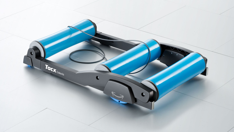 Rullo per allenamento bici Tacx Galaxia con tre rulli blu in un telaio nero su pavimento chiaro.