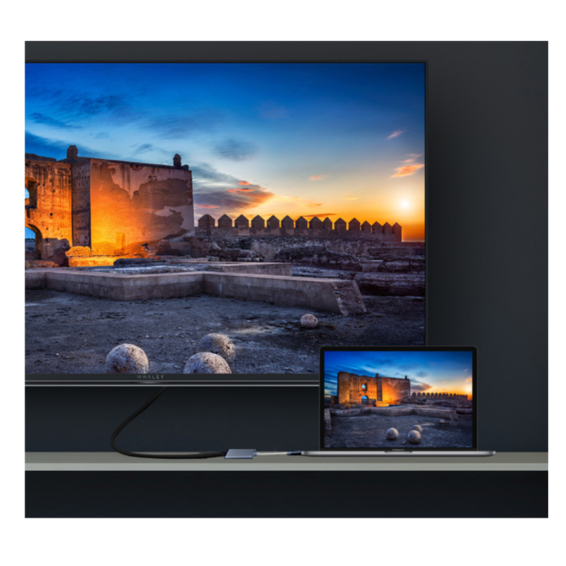 Un ordenador portátil está conectado a un monitor mediante un cable, ambos muestran la imagen de una ruina antigua al atardecer.