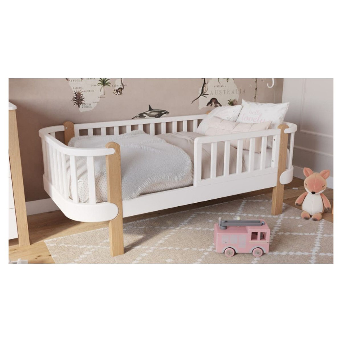 Weißes Kleinkinderbett mit Holzbeinen, Kissen, Decke, Teppich, rosa Spielzeugauto und Kuscheltier im Kinderzimmer.