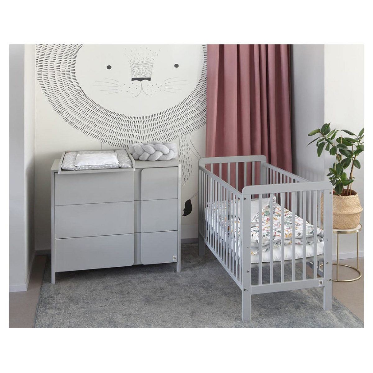 Graues Babybett und passende Kommode vor einer Wand mit Löwenzeichnung und rosa Vorhängen.