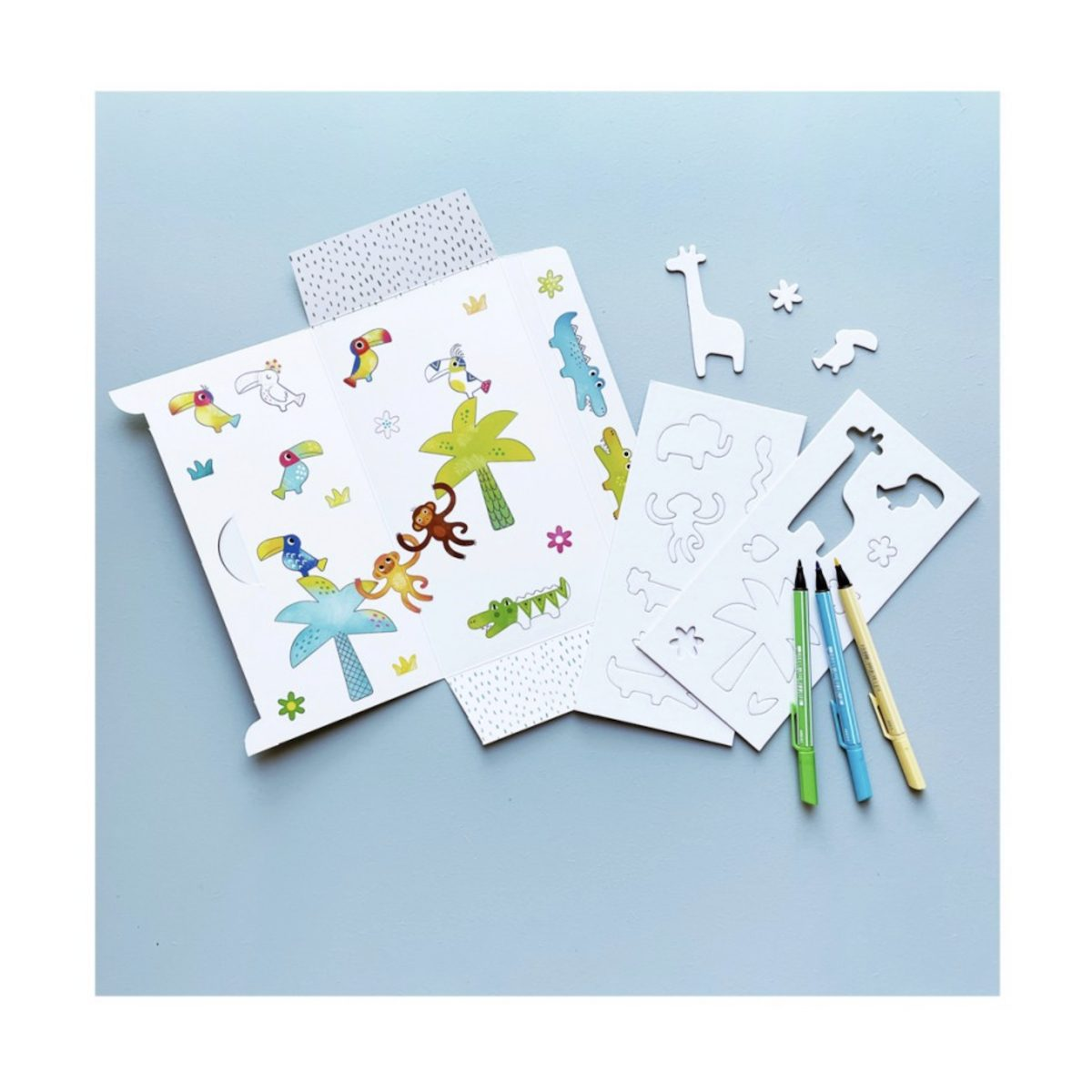 Bastelset mit bedrucktem Papier, Schablonen, Ausschnitten und drei Buntstiften auf blauem Hintergrund.