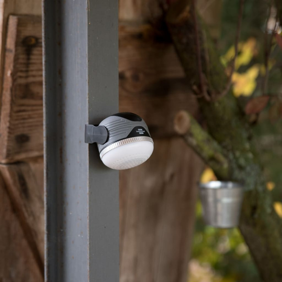 Eine kleine graue und weiße LED-Lampe ist an einem Metallträger vor einer holzverkleideten Wand befestigt.