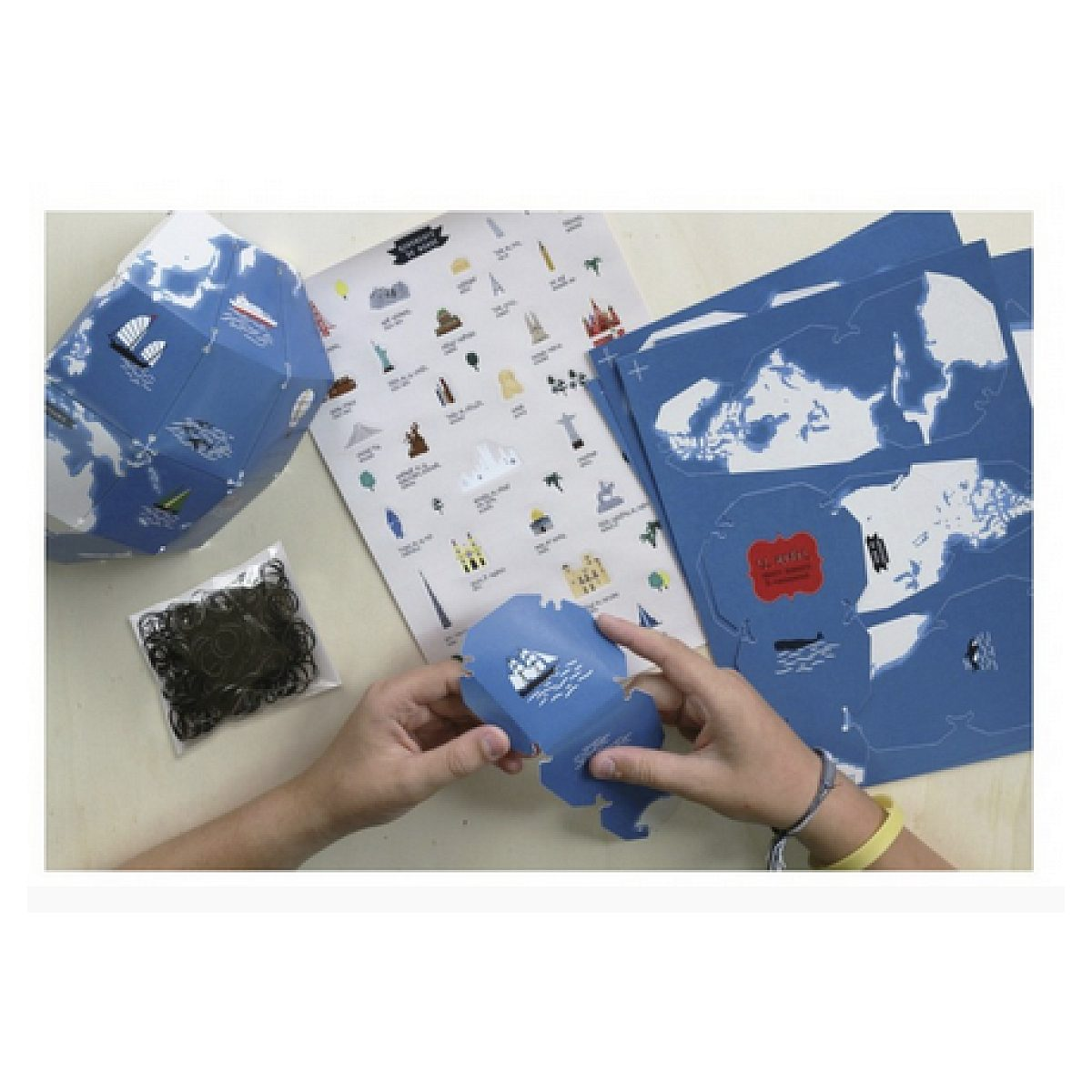 Hände bauen ein blaues Papierglobus-Bastelset mit Anleitung und Gummibändern.