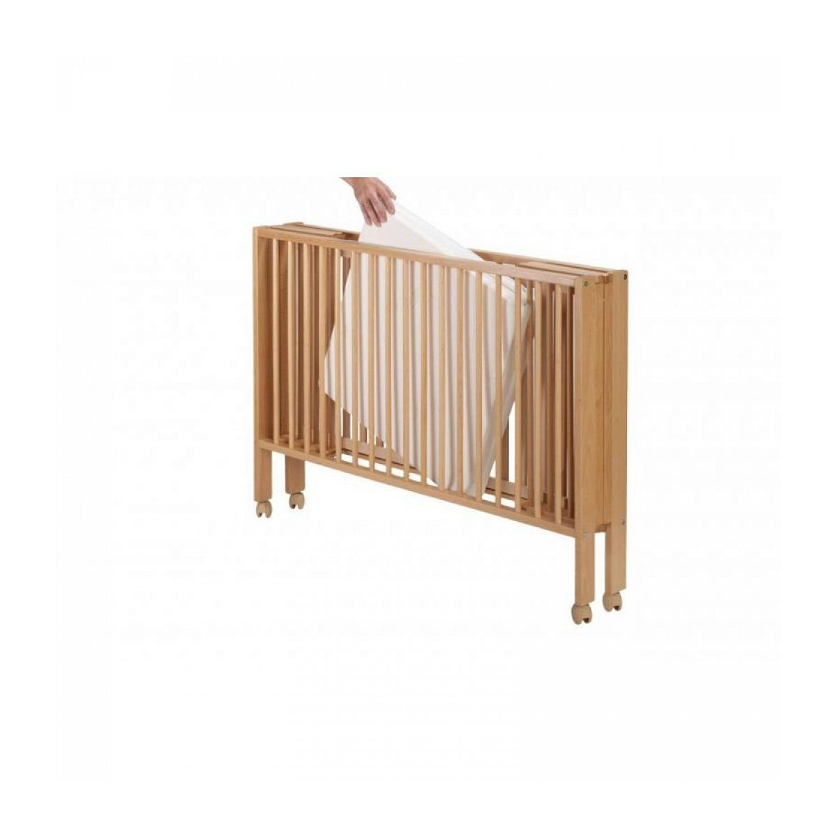 Eine Hand legt eine helle Matratze in ein zusammengeklapptes Holzbabybett auf Rollen.