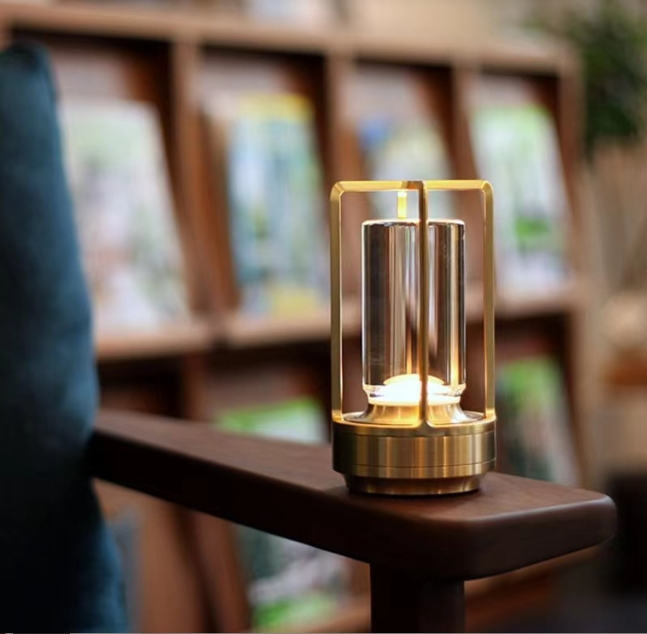 Een kleine messing lamp met glazen cilinder staat op een houten armleuning, met een plank op de achtergrond.