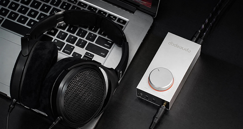 Czarne słuchawki otwarte leżą na laptopie obok srebrnego wzmacniacza audio.