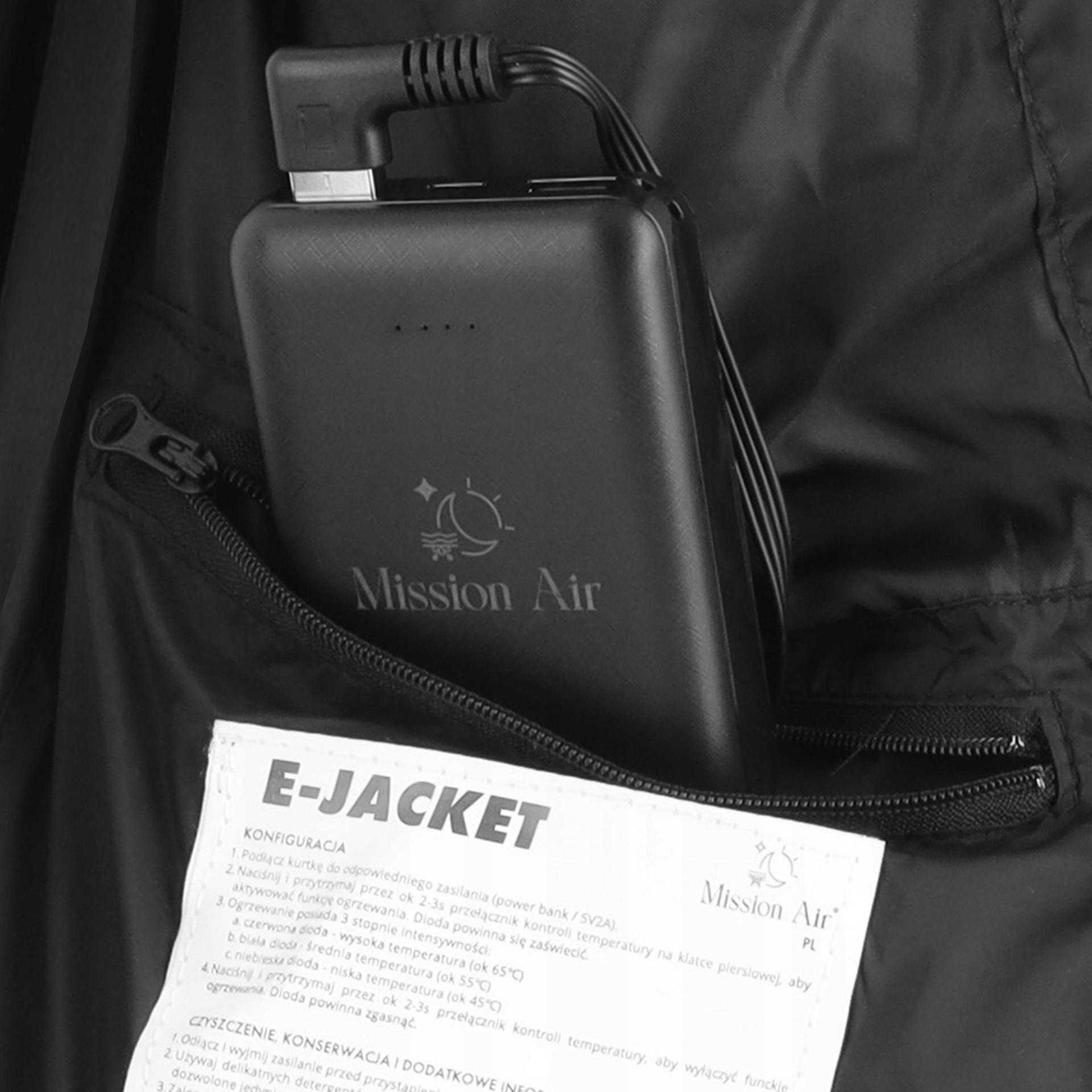 Czarny powerbank z logo Mission Air w kieszeni kurtki, z podłączonym kablem i instrukcją E-Jacket.