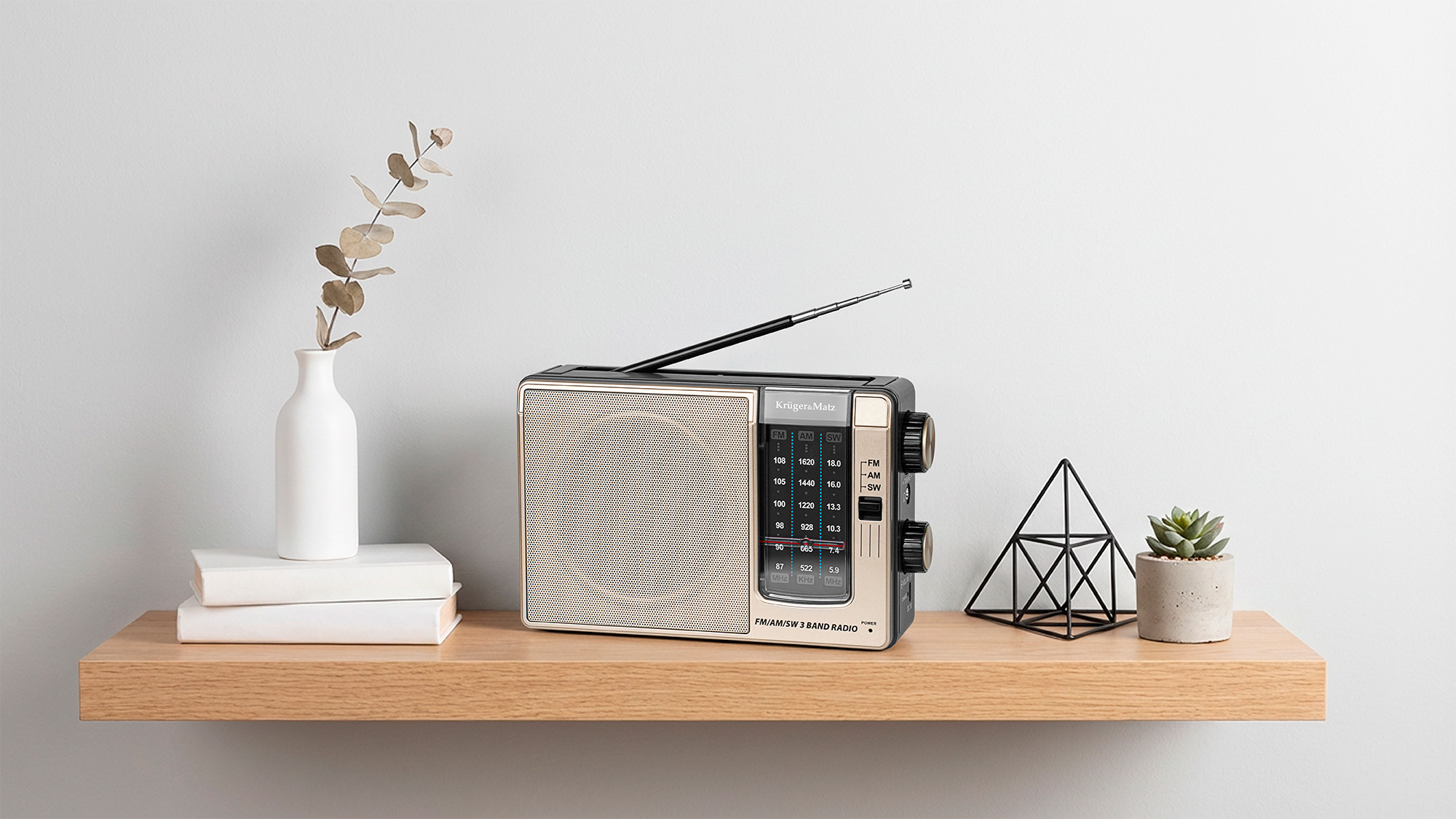 Beżowo-czarne radio retro na drewnianej półce z dwoma białymi książkami, wazonem i małą rośliną.
