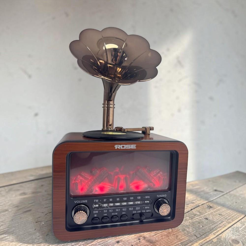 Ahşap masada duran, şömine ekranlı ve pembe altın gramofon hunili ahşap bir retro radyo.