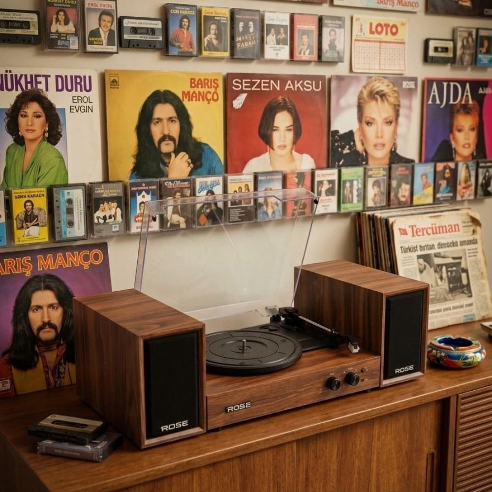 Ahşap kaplamalı iki hoparlörlü bir Rose pikap, kasetler ve müzik posterleriyle kaplı bir duvarın önündeki masada duruyor.