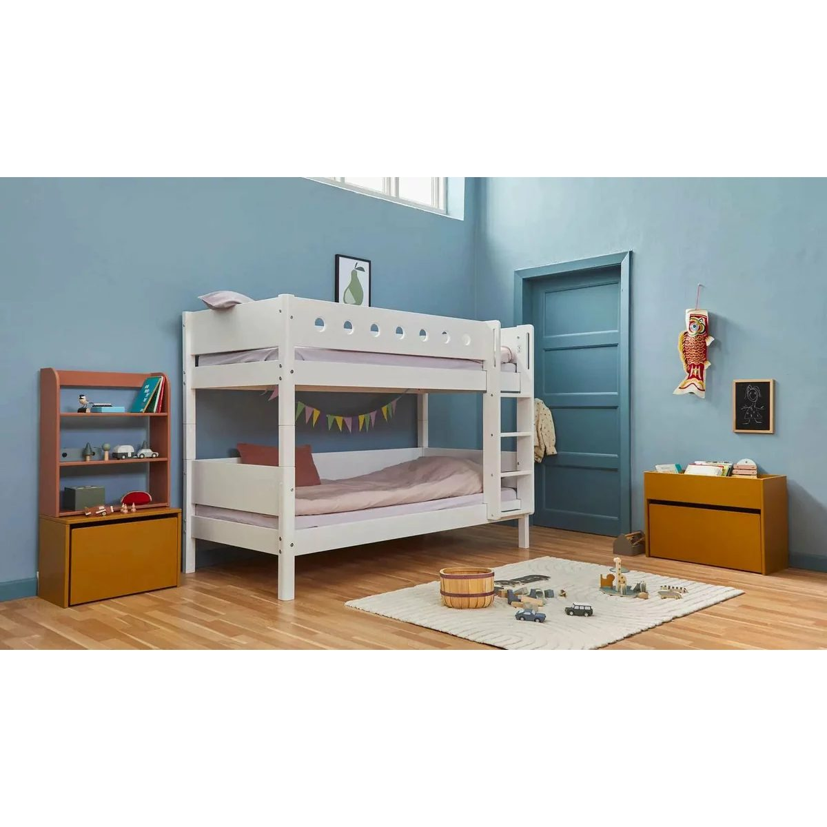 Ein weißes Etagenbett in einem blauen Kinderzimmer mit Holzmöbeln, Spielzeug und einem Teppich auf dem Holzboden.