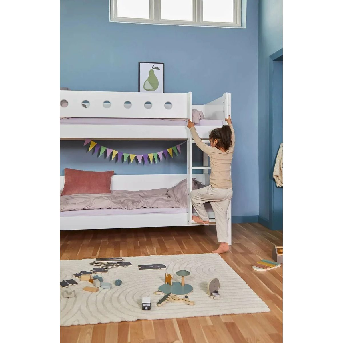Ein Kind klettert in einem blauen Zimmer auf ein weißes Etagenbett mit hellem Teppich.