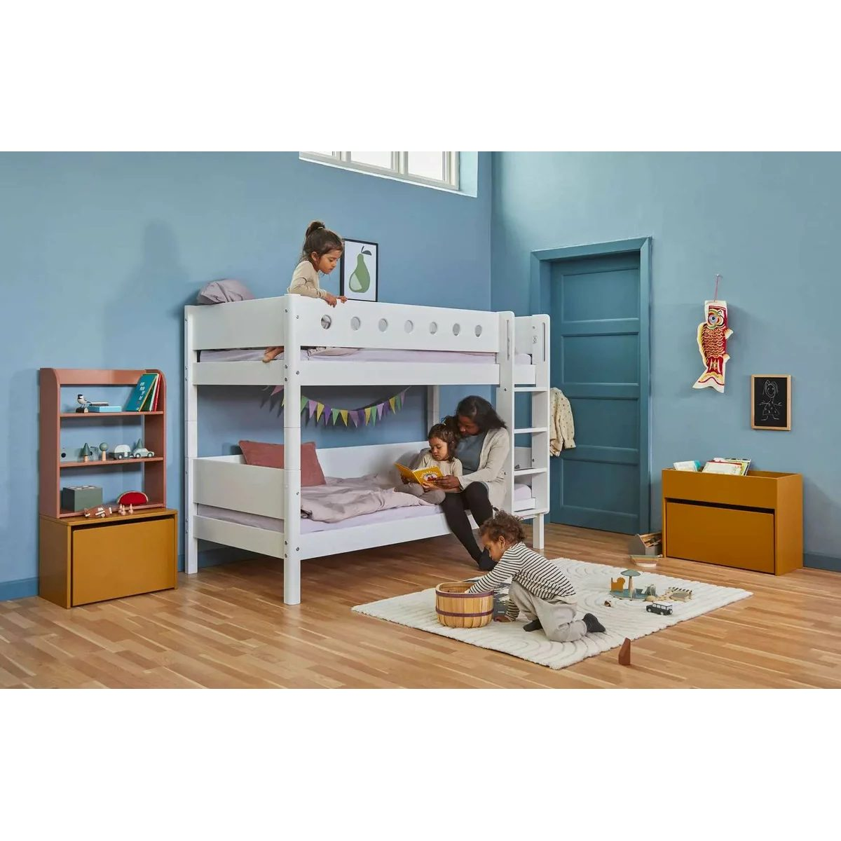Eine Frau liest Kindern in einem hellen Kinderzimmer mit weißem Etagenbett ein Buch vor.