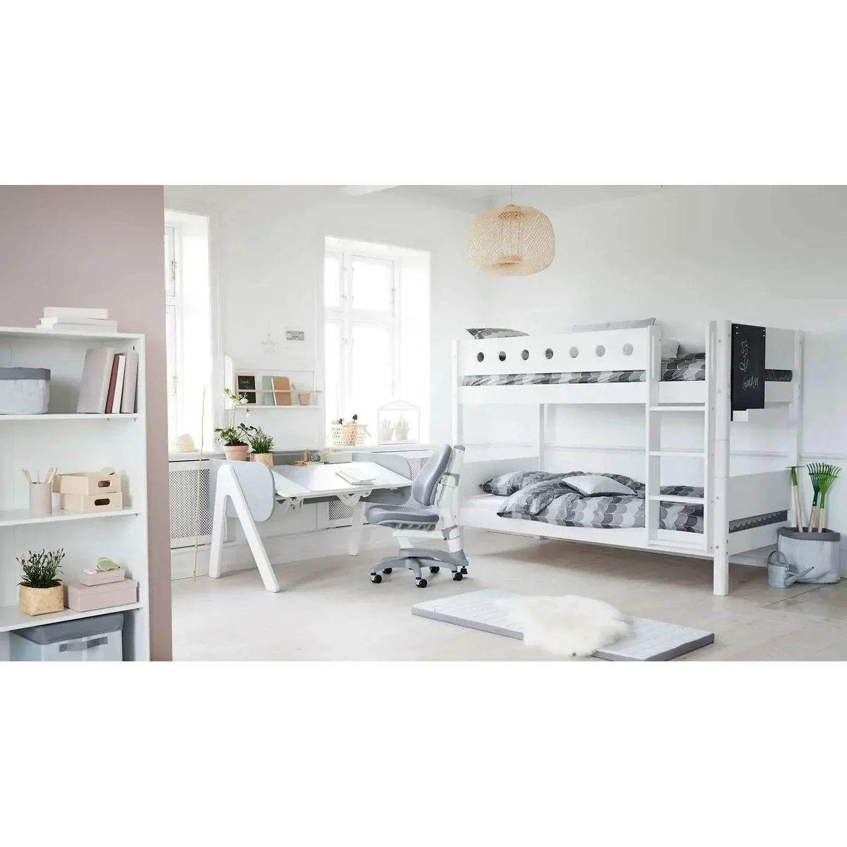 Helles Kinderzimmer mit weißem Etagenbett, Schreibtisch, Rollstuhl, Regal und großen Fenstern.