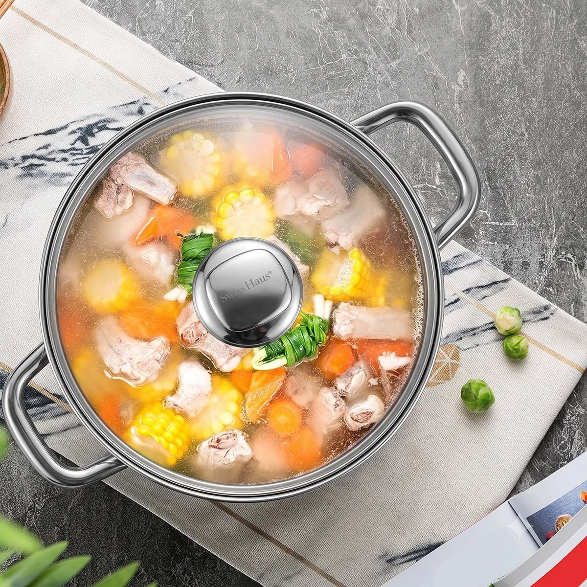 Ein geschlossener Edelstahltopf mit Suppe, Mais, Fleisch und Karotten auf einem Tuch.