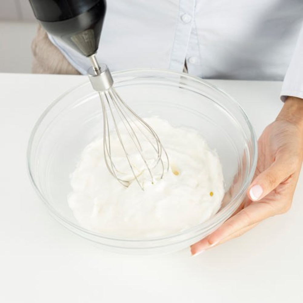 Persona che mescola impasto bianco in una ciotola di vetro.