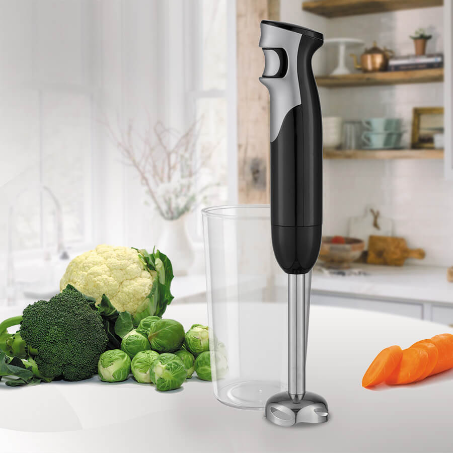 Czarno-srebrny blender ręczny stoi obok wysokiego kubka, kalafiora, brokuł ów, brukselki i plasterków marchewki.