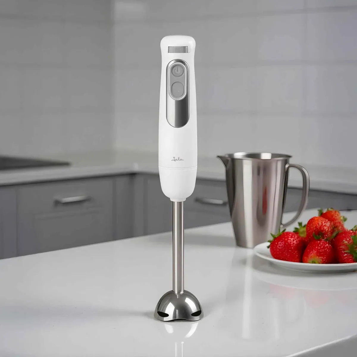 Una batidora de mano blanca sobre una encimera de cocina junto a una jarra y fresas.