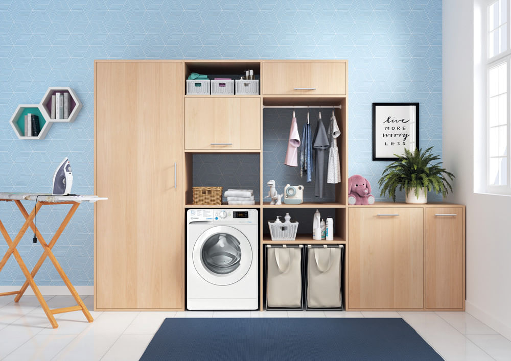 Moderna lavanderia con mobili in legno, lavatrice bianca, vestiti appesi e pareti con motivi blu.