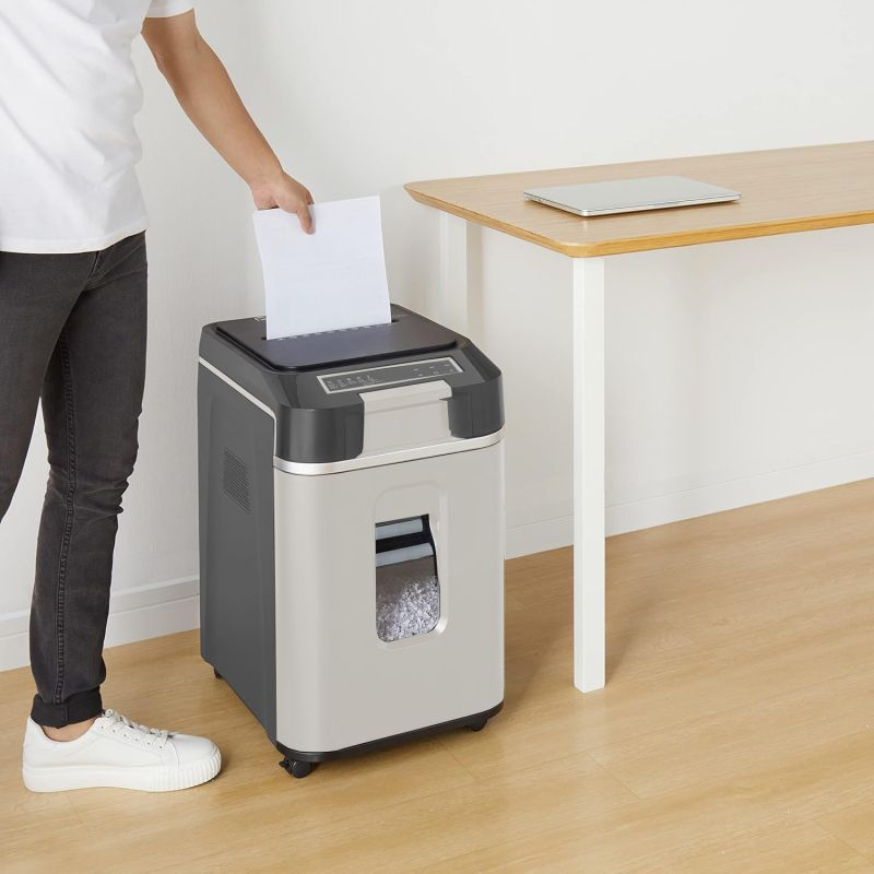 Eine Person steckt Papier in einen silbernen Aktenvernichter neben einem Holztisch in einem Büro.