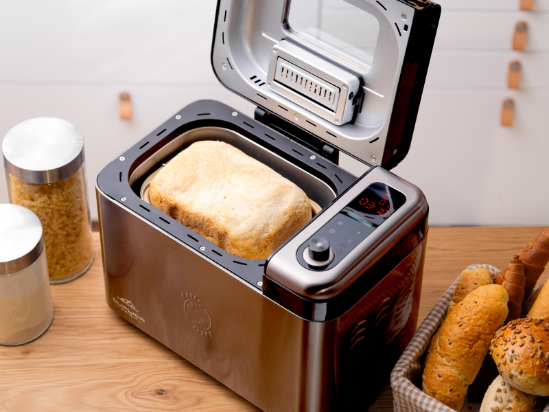 Ein offener Edelstahl-Brotbackautomat mit frisch gebackenem Brot im Inneren, daneben Brotkörbe und Vorratsdosen.