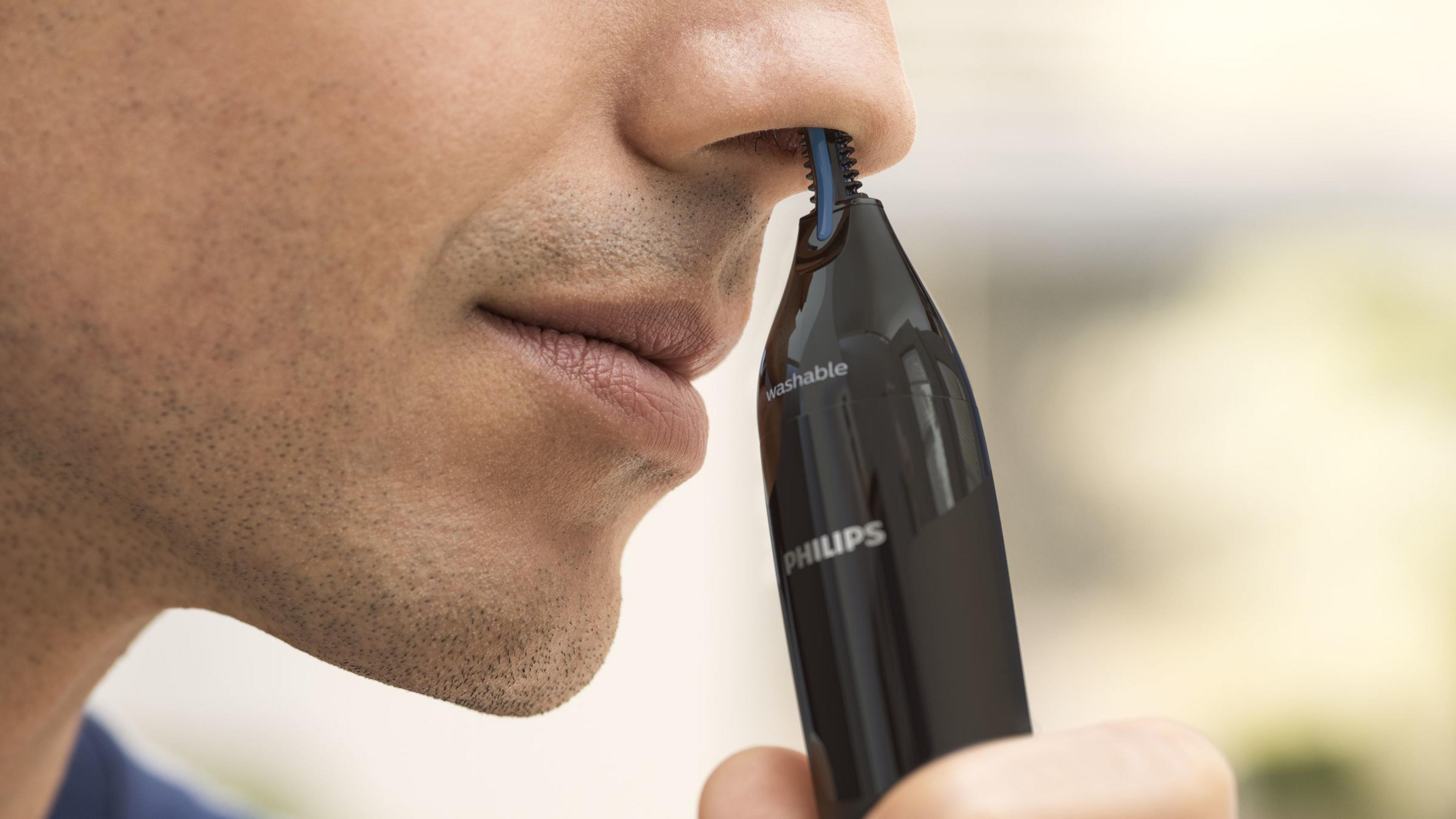Un uomo usa un rifinitore per peli nasali Philips nero per regolare i peli nelle narici.