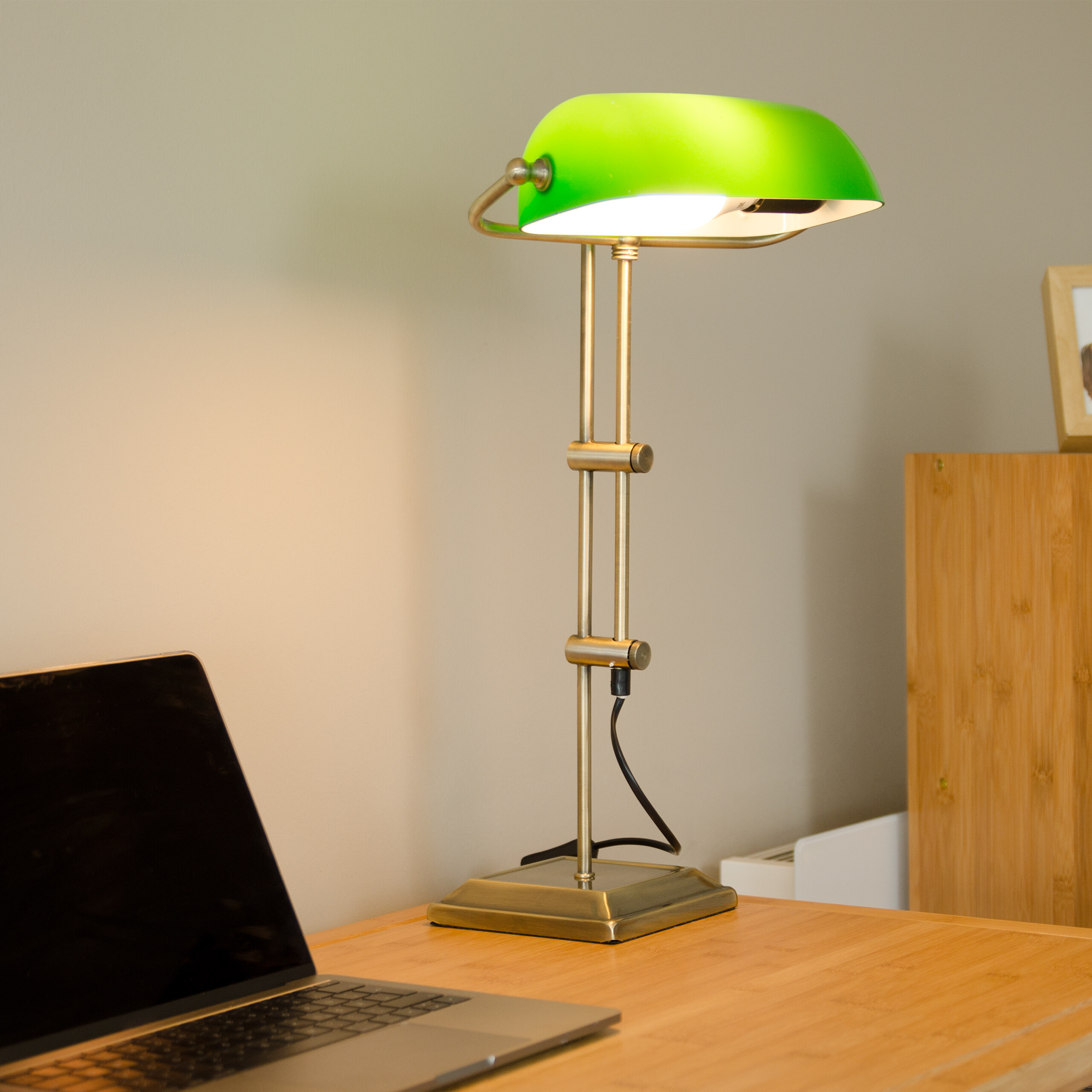 Eine grüne Schreibtischlampe leuchtet auf einem Holztisch neben einem Laptop.