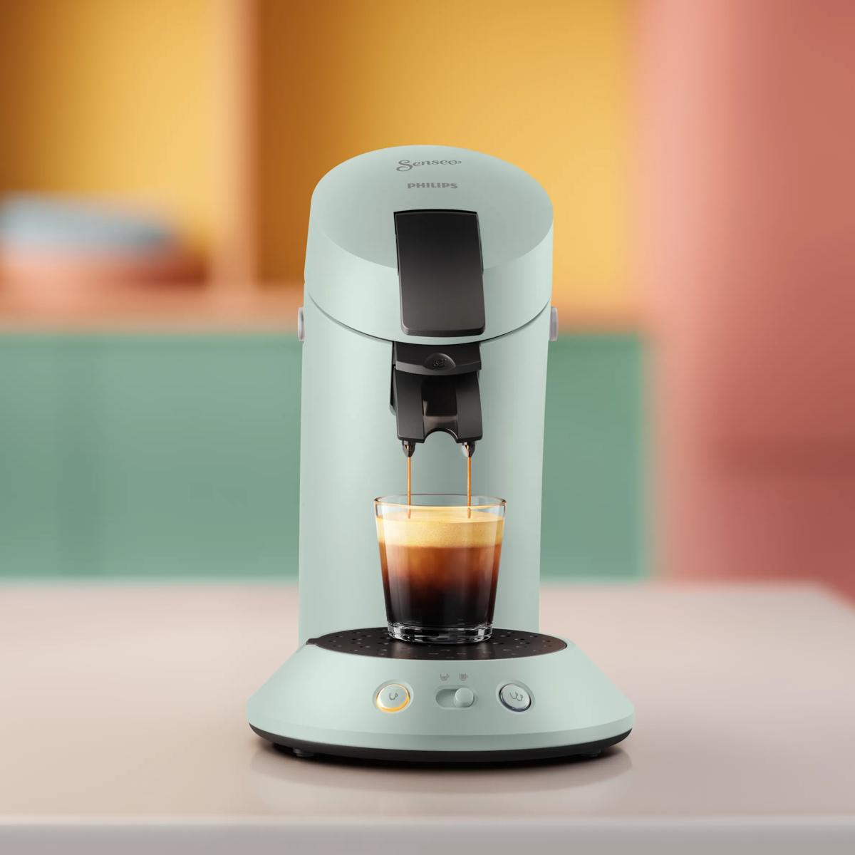 Una macchina da caffè Senseo Philips verde menta eroga caffè in un bicchiere sul bancone.