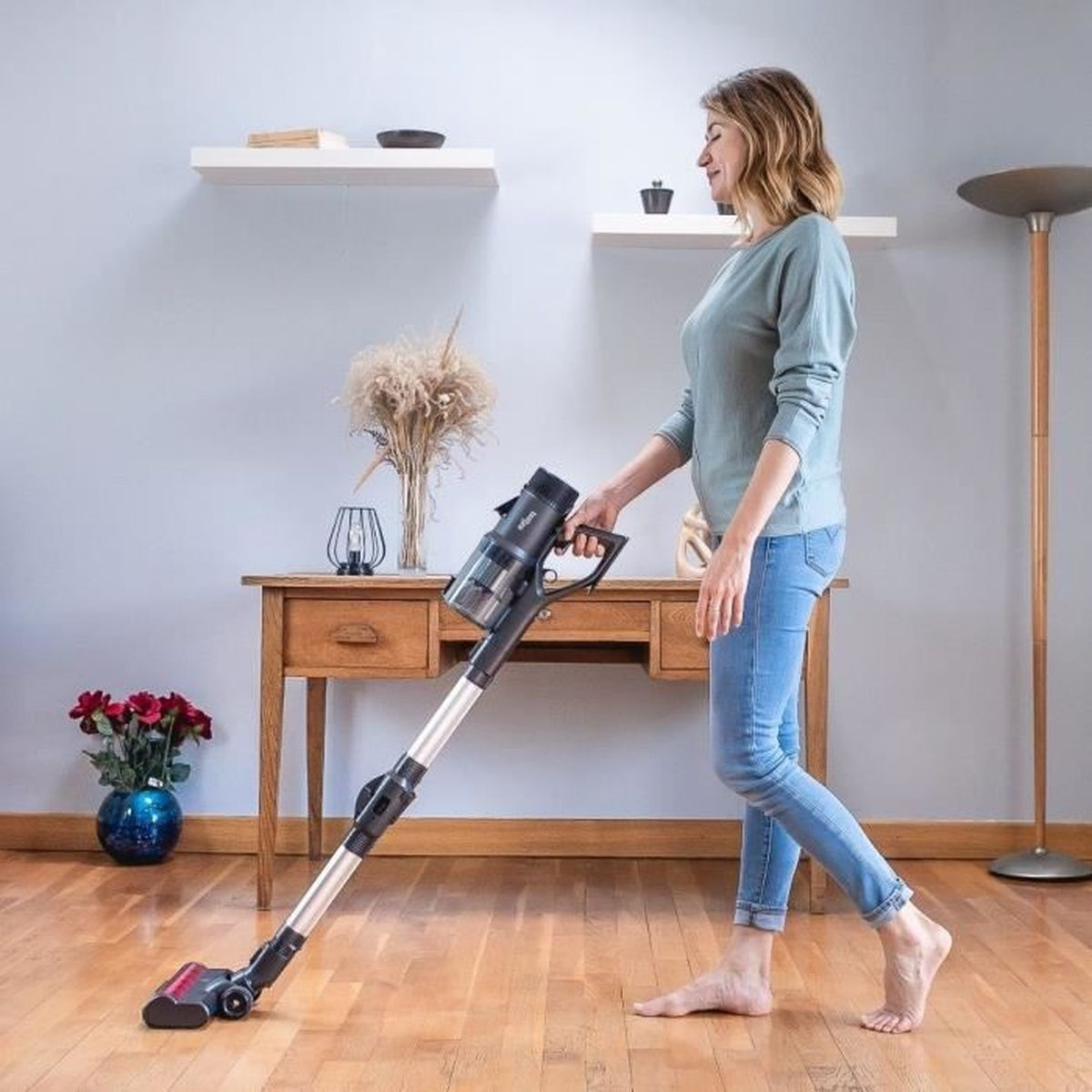 Eine Frau in Jeans und Pullover saugt mit einem kabellosen Staubsauger einen Parkettboden.