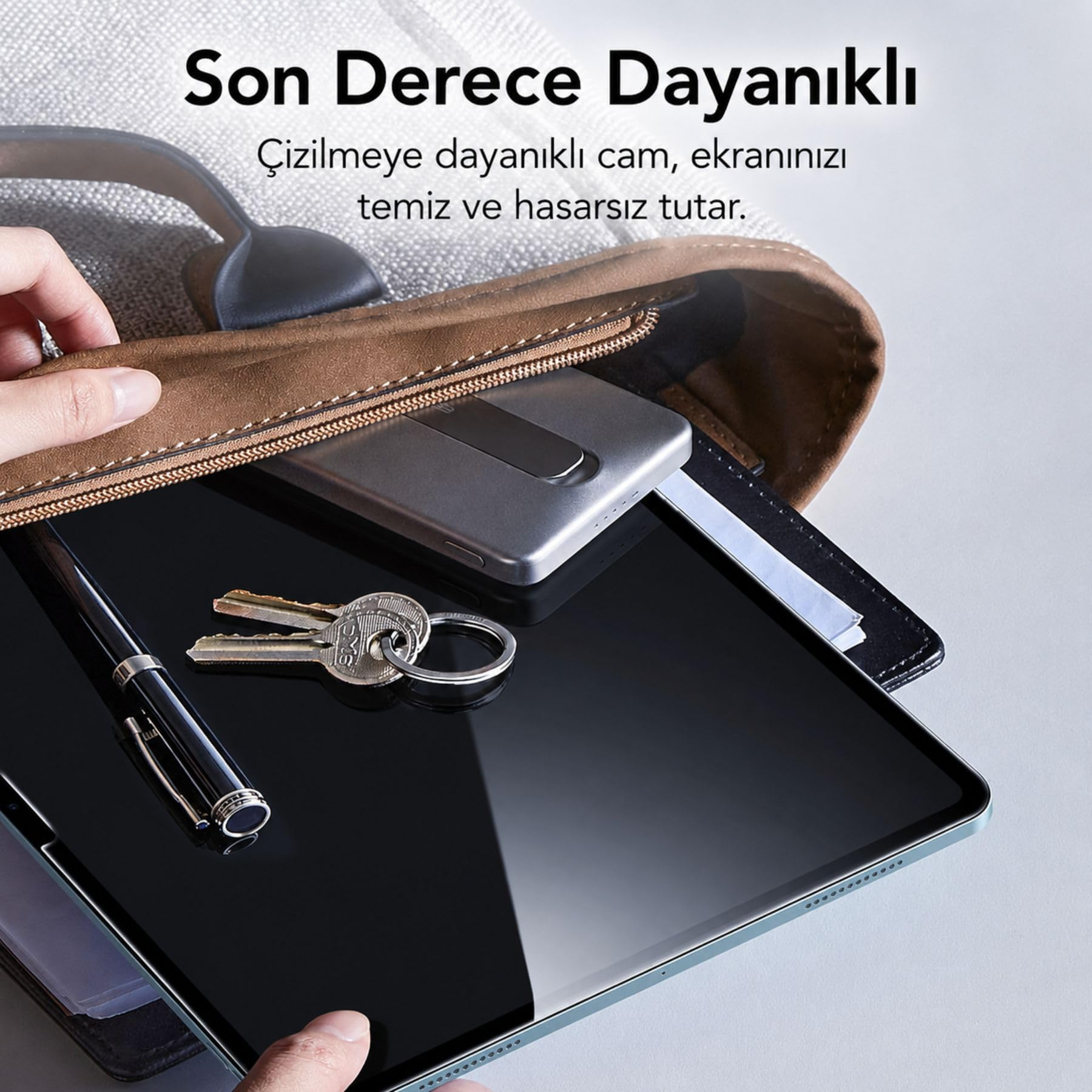 Kalem ve anahtarların bulunduğu bir tablet, akıllı telefonun yanında açık bir çanta içindedir.