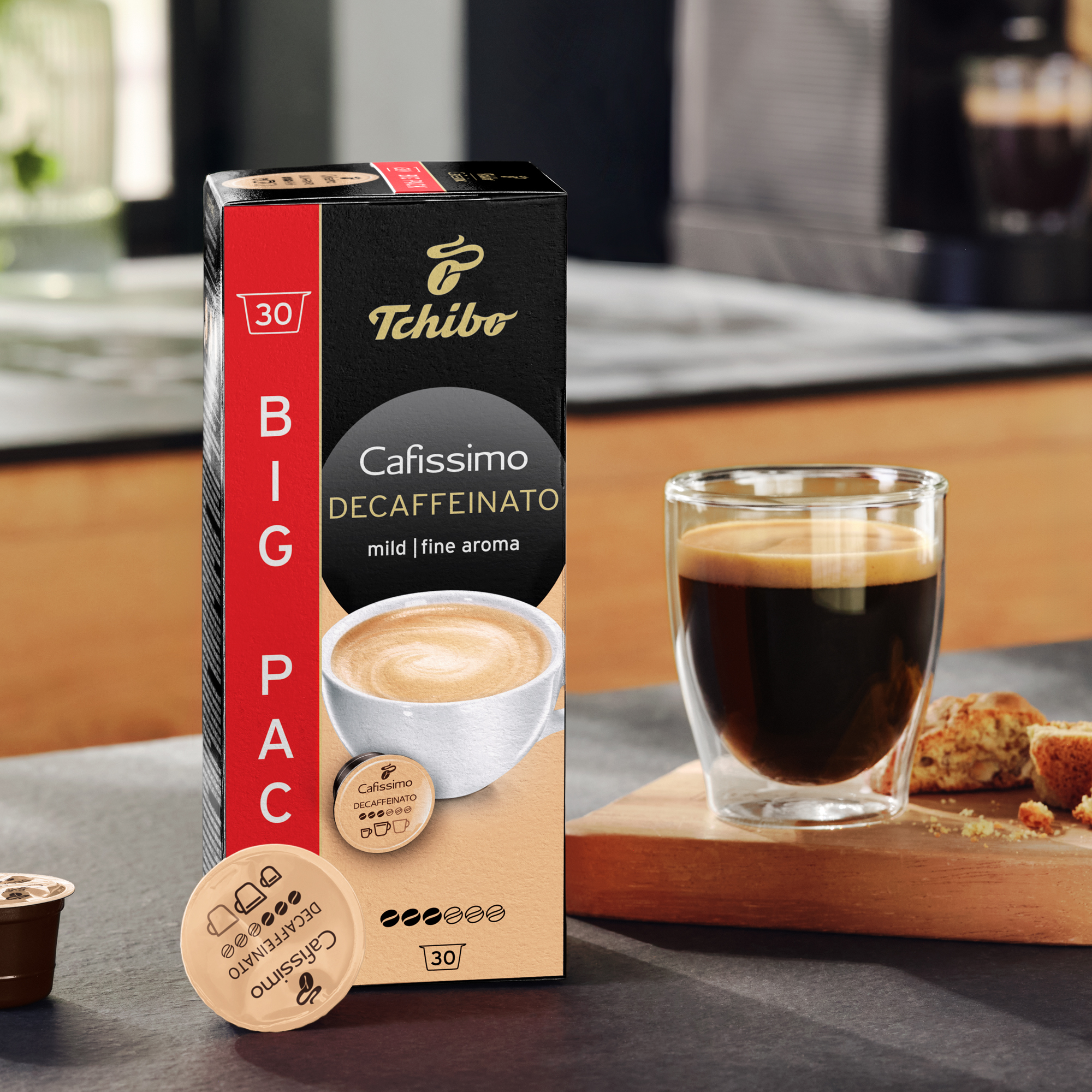 Tchibo Cafissimo Decaffeinato Kaffee-Box mit Kapseln, einer Kaffeetasse und Gebäck auf einem Holbrett.