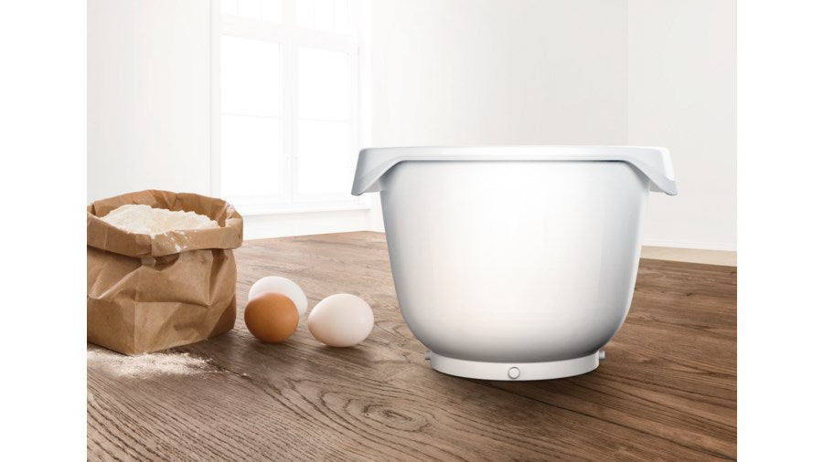 Un bol blanco, una bolsa de harina y tres huevos sobre una mesa de madera.