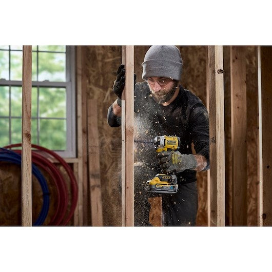 Un trabajador con gorro gris taladra un marco de madera mientras vuelan virutas.