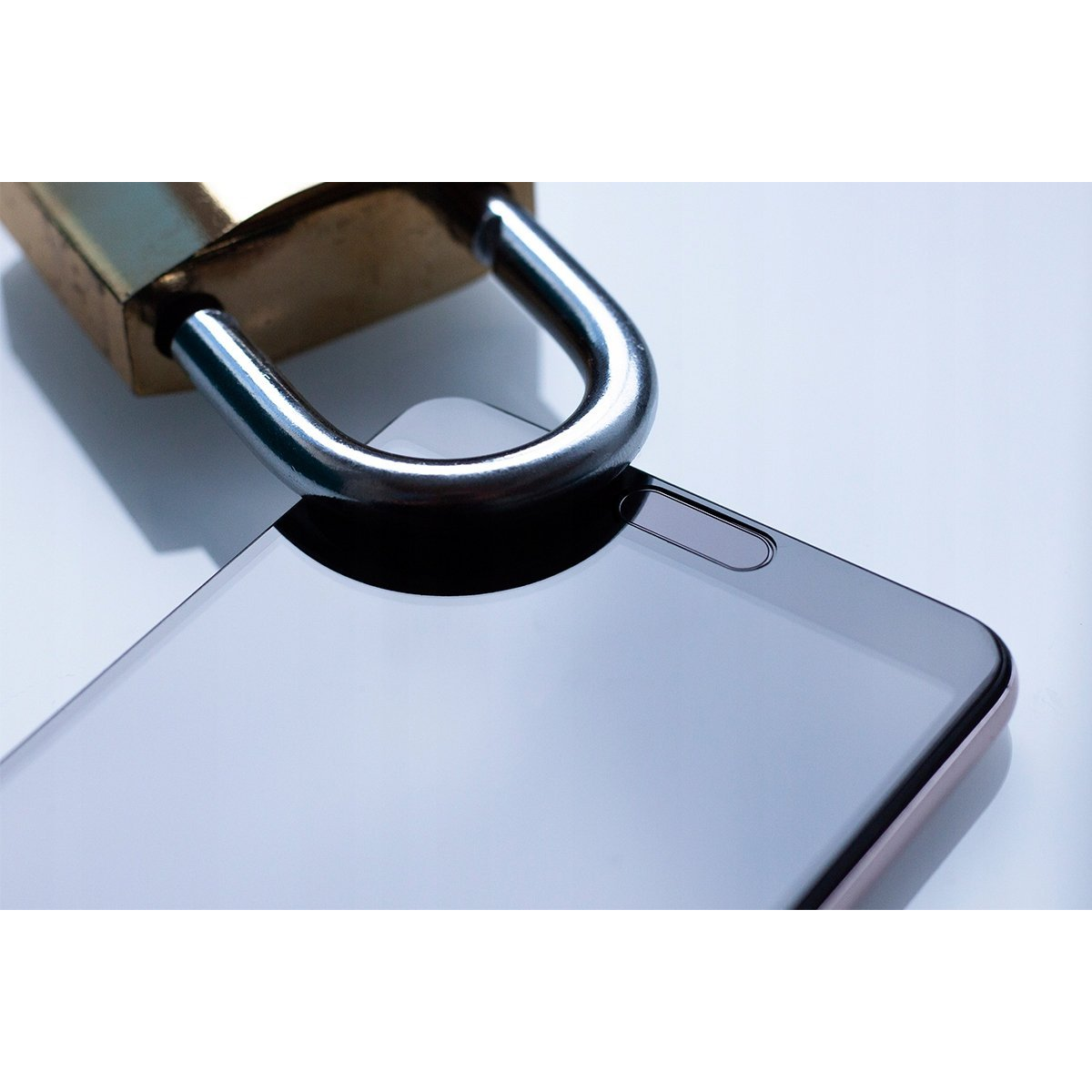Primer plano de un candado plateado sobre la esquina de la pantalla de un smartphone negro en superficie blanca.
