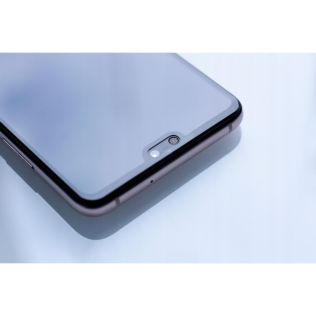 Primer plano de la parte superior de un smartphone moderno con cámara y altavoz sobre un fondo claro.