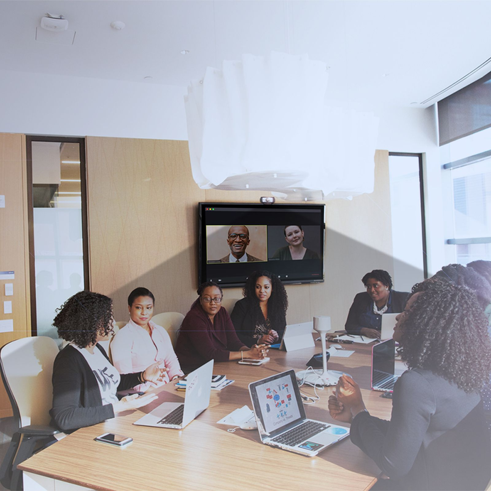 Un gruppo diversificato di colleghi siede a un tavolo in una moderna sala riunioni, partecipando a una videoconferenza.