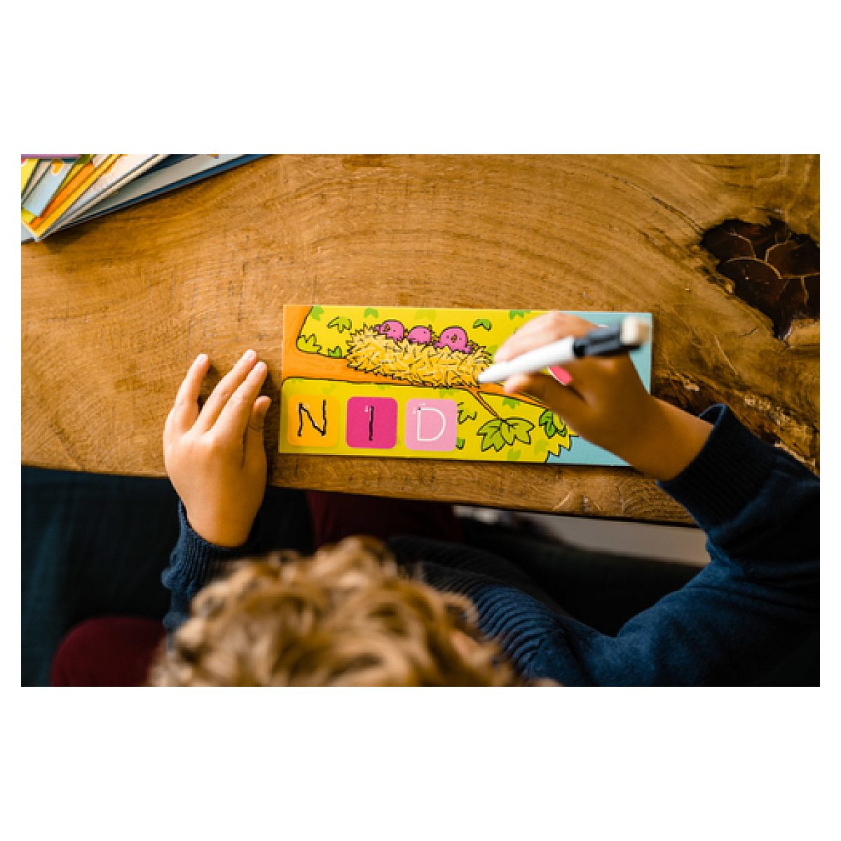 Ein Kind schreibt mit einem Stift auf ein buntes Papier mit Buchstaben.