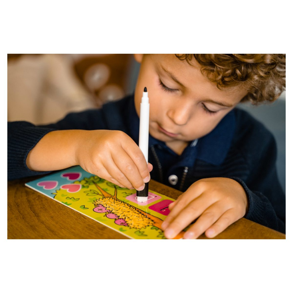 Ein Junge mit lockigem Haar zeichnet mit einem Stift auf ein buntes Bild.