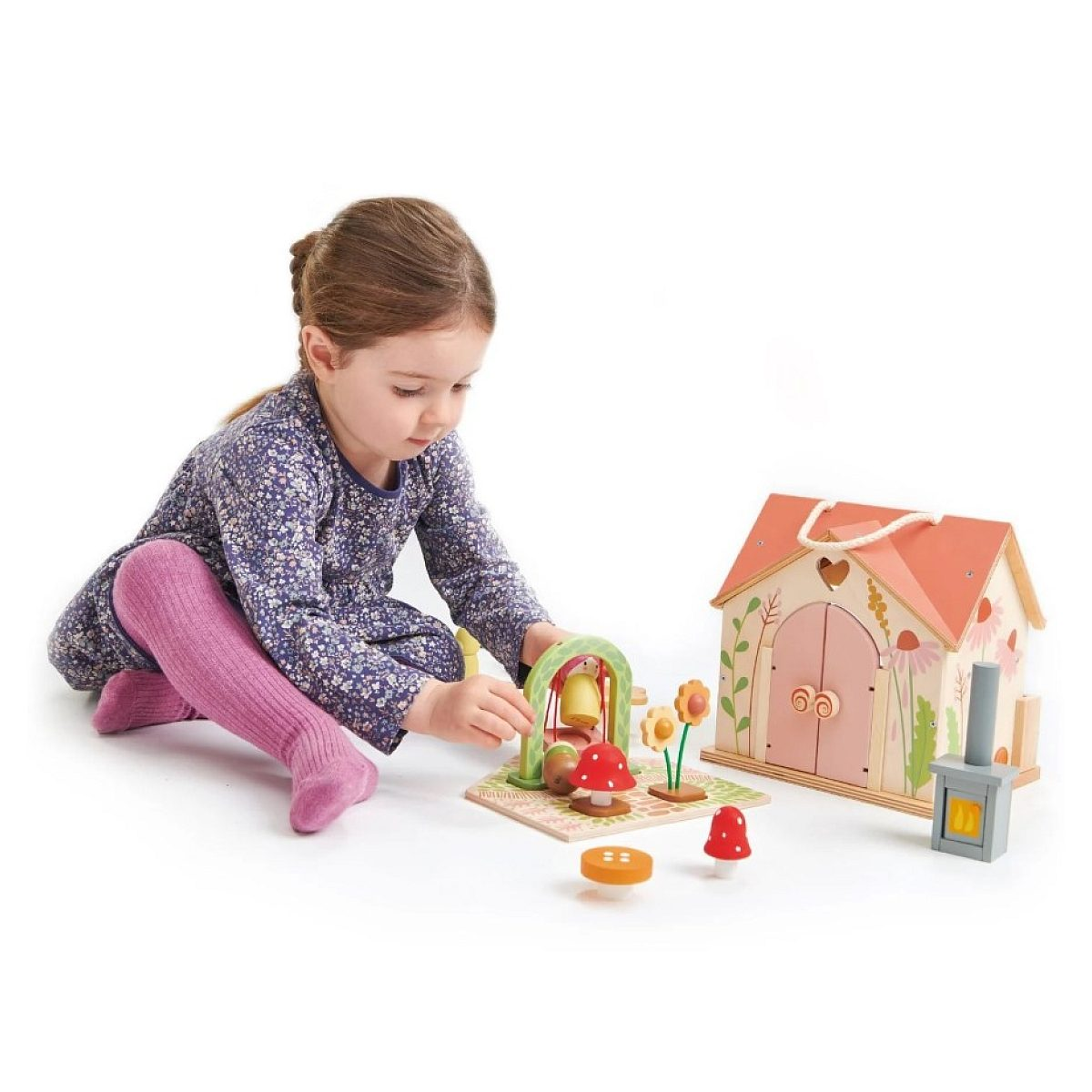Ein Mädchen spielt auf dem Boden mit einem Holzspielzeugset, das ein Haus und Figuren enthält.