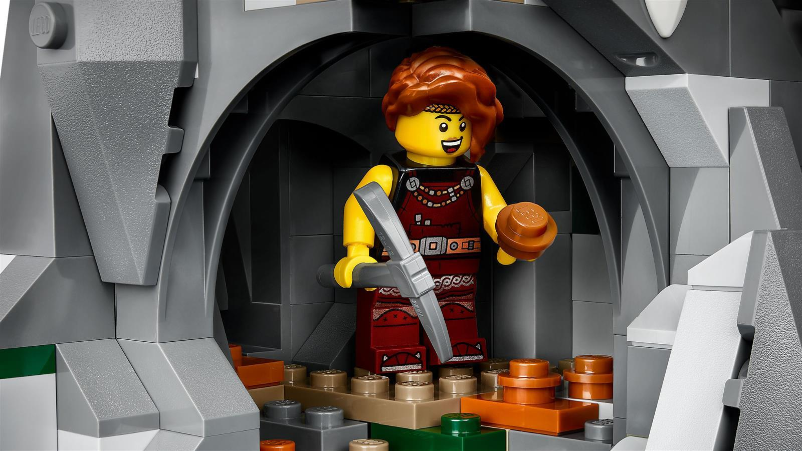 Eine LEGO-Minifigur mit roten Haaren steht in einer grauen Steinhöhle und hält eine Spitzhacke und ein braunes Stück.