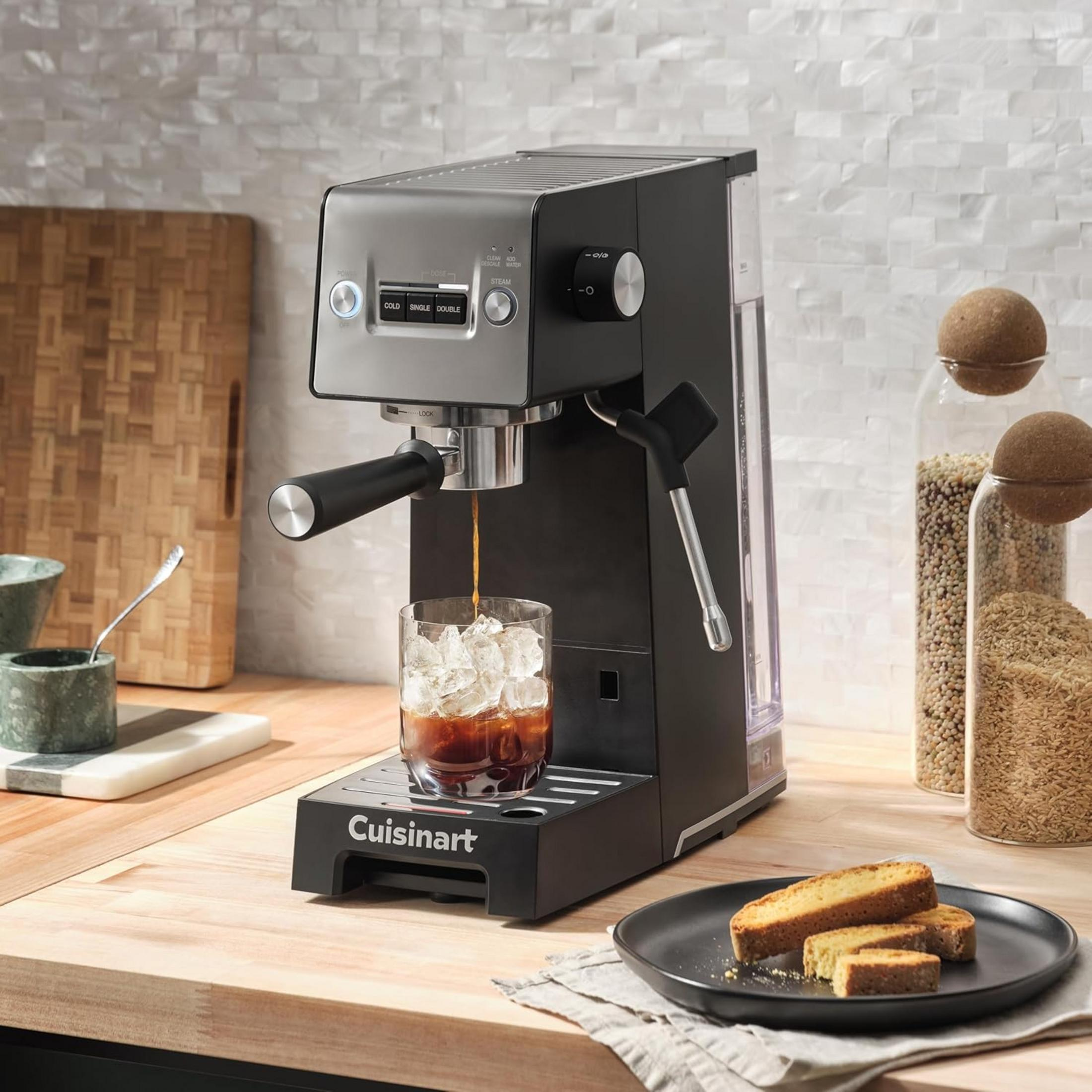 Una macchina da caffè Cuisinart nera e argento eroga caffè in un bicchiere con ghiaccio su un bancone di legno.