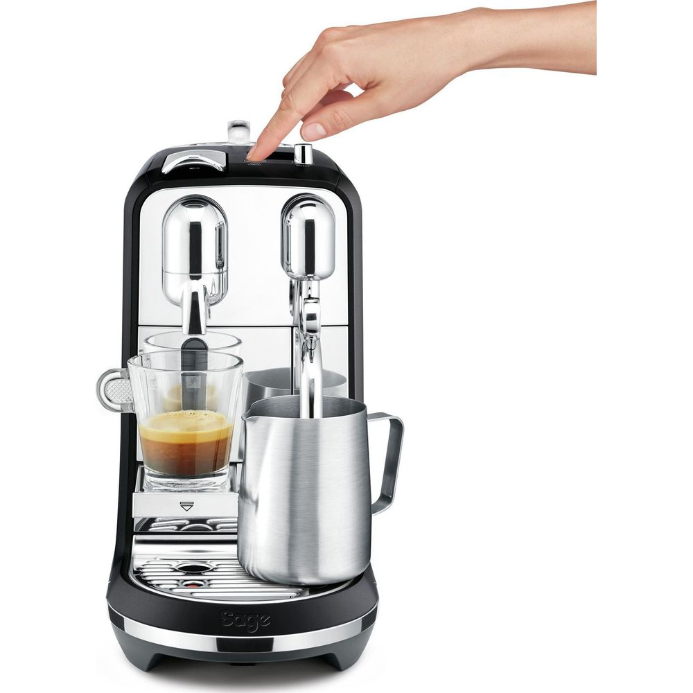 Main appuyant sur le bouton d'une cafetière noire et argentée avec tasse et pichet.