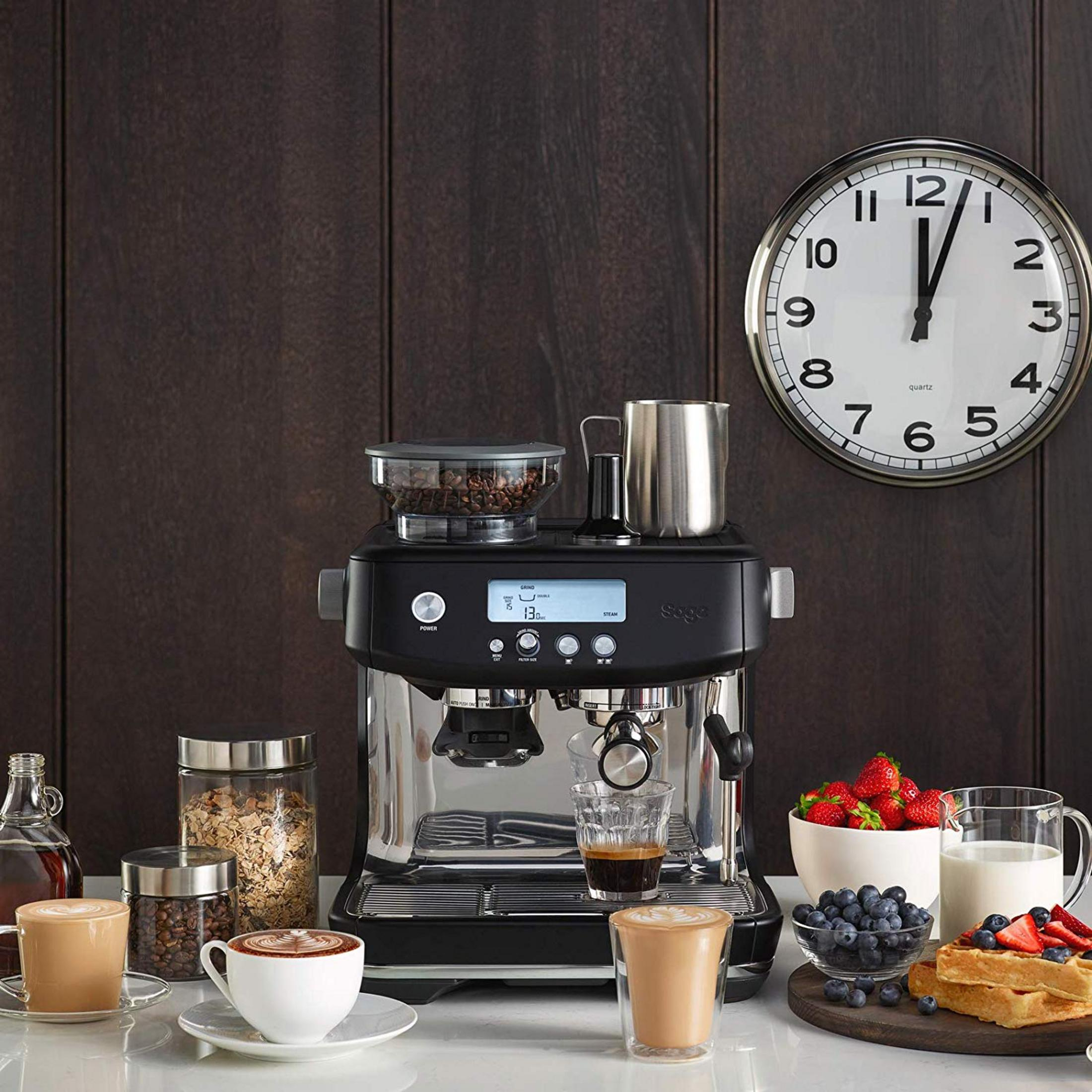 Machine à espresso noire avec tasses, baies, lait, gaufres et horloge murale sur bois foncé.