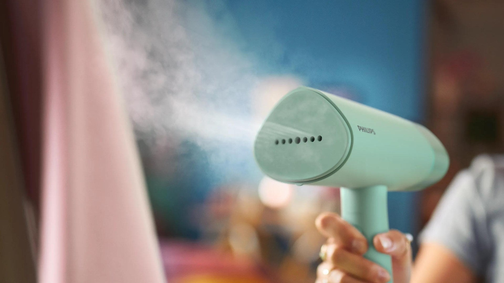 Hand gehaltenes mintgrünes Philips-Dampfbügeleisen, das Dampf auf ein rosa Kleidungsstück sprüht.