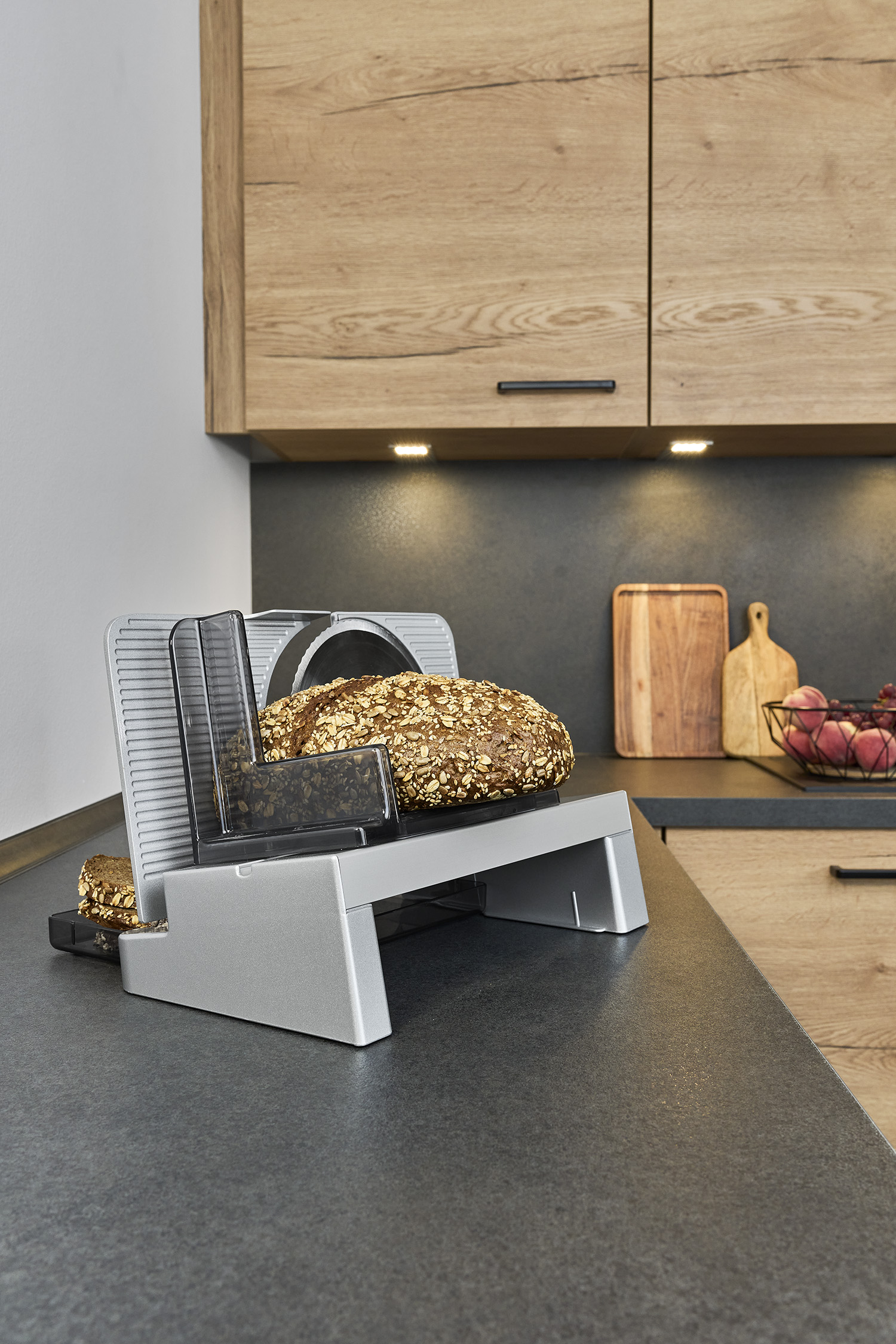 Un'affettatrice elettrica per pane con una pagnotta di pane ai semi su un bancone da cucina scuro.