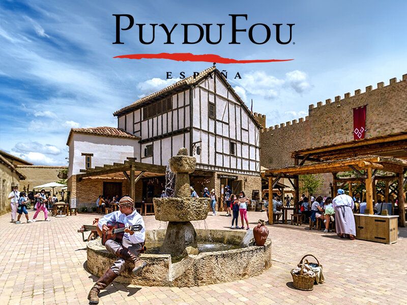 Un guitarrista se sienta junto a una fuente en el pueblo histórico de Puy du Fou España bajo un cielo azul.