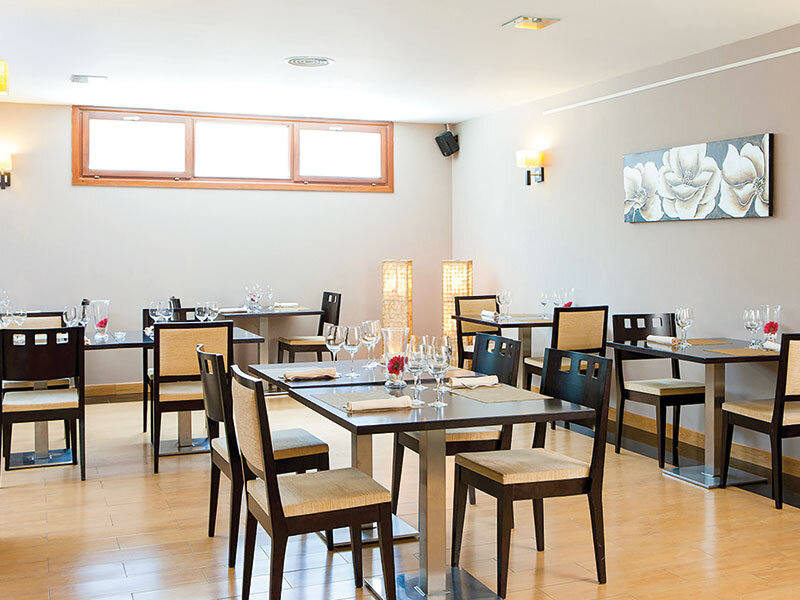 Interior de restaurante acogedor con mesas de madera oscura, sillas tapizadas y luz suave sobre paredes beige.