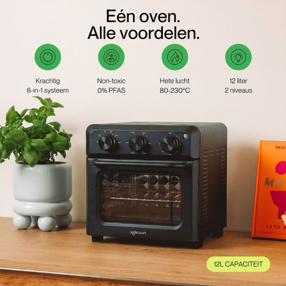 Black mini oven on a wooden table with a potted plant, orange book, and green feature icons.